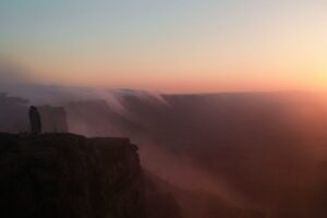Two people stand on a cliff at sunset